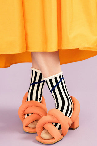 Close-up of women's legs wearing orange dress, orange shoes and black and white Chelsea rolled top crew sock by Hansel from Basel. 