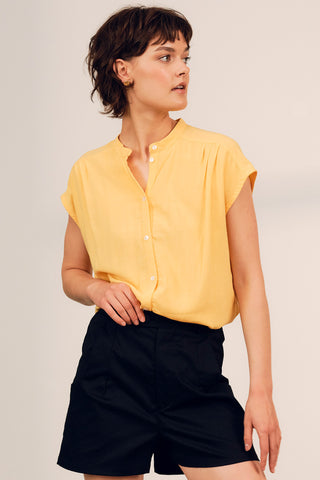Woman wearing yellow mandarin collar button up Lyra top by Jennifer Glasgow. 