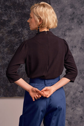 Back view of model wearing black mock neck 3/4 length sleeve Maeve top by Jennifer Glasgow. 