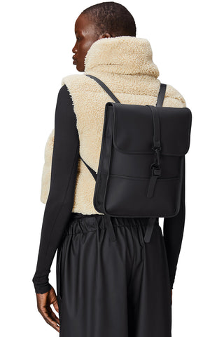 Woman wearing fuzzy jacket with waterproof black Micro W3 Backpack by Rains. 