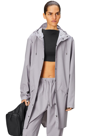 Woman wearing grey flint coloured waterproof Long Jacket by Rains. 
