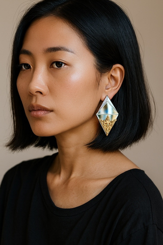 Side view of woman wearing silver plexiglass diamond shape earring with gold filigree detail. 