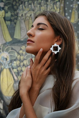 Woman with closed eyes wearing silver mirror plexiglass geometric shape earrings. 