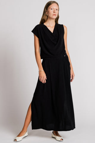 Woman wearing black asymmetrical tank top with matching maxi skirt with side slit. 