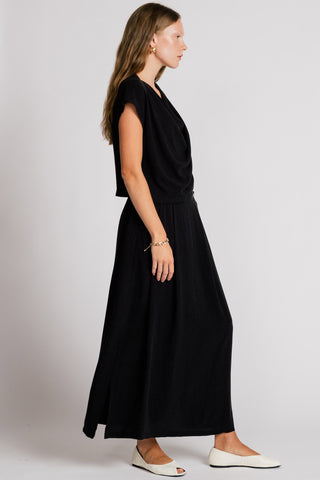 Side  view of woman wearing black asymmetrical tank top with matching maxi skirt. 