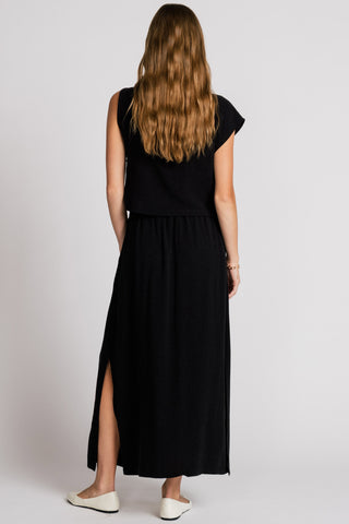 Back view of woman wearing black asymmetrical tank top with matching maxi skirt with side slit. 