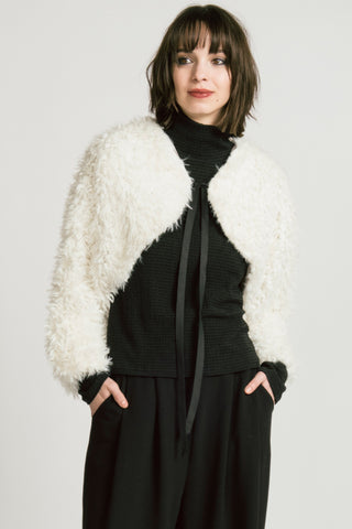 Woman wearing black mock neck top and black pants, with white fuzzy bolero over top.