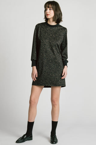 A model wearing a black long-sleeve crewneck dress with leopard print, paired with black socks and black leather loafers, against a light gray studio background.