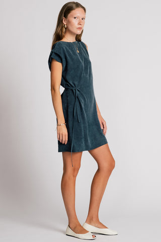 Woman in front of white background wearing dark blue asymmetrical cut above the knee summer dress. 