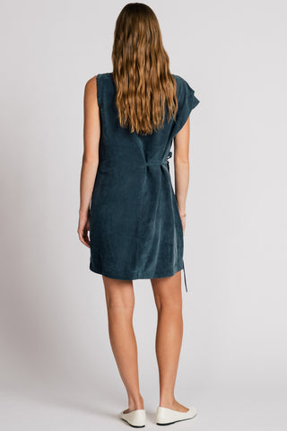 Back view of woman in front of white background wearing dark blue asymmetrical cut above the knee summer dress. 