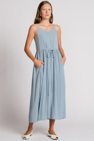 Woman wearing light blue maxi dress with drawstring waist and front pockets. 