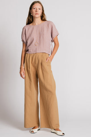 Woman in front of white background wearing a pink gingham blouse and wide leg tan pants. 