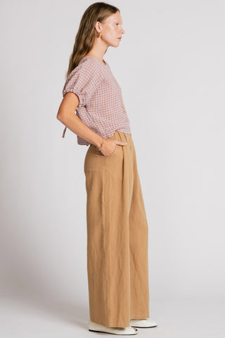 Woman in front of white background wearing a pink gingham blouse and wide leg tan pants. 
