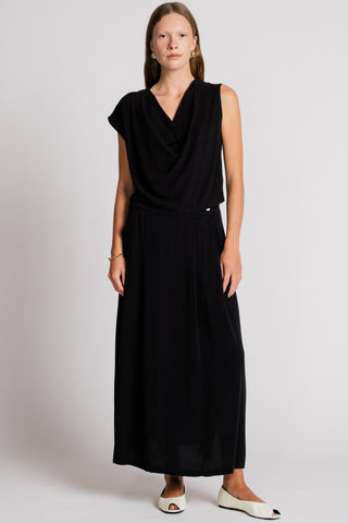 Woman wearing black tank top and long black skirt in front of grey background. 
