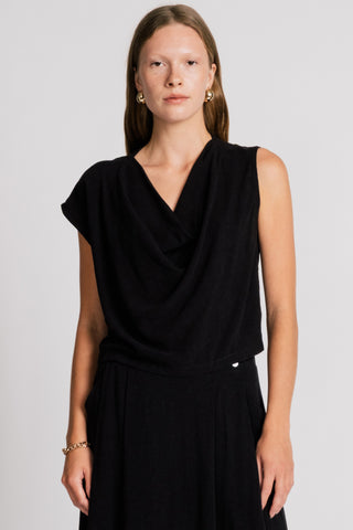 Woman wearing black asymmetric tank top in front of white background. 