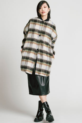 Model in front of grey background wearing mid-thigh length plaid Dizzy coat by Allison wonderland, with black pleather skirt and black Chelsea boots. 
