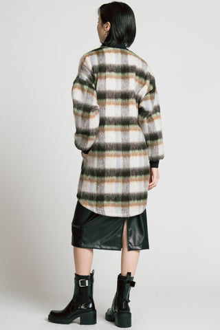 Back view of model in front of grey background wearing mid-thigh length plaid Dizzy coat by Allison wonderland, with black pleather skirt and black Chelsea boots. 