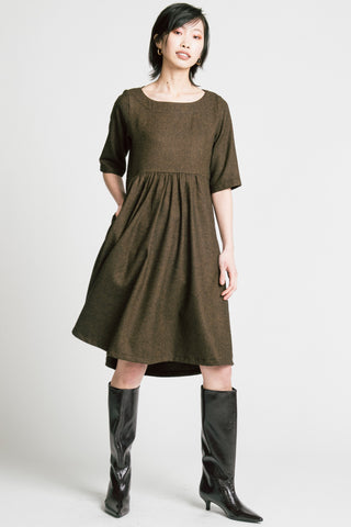 Woman standing in front of grey background wearing brown herringbone llison Wonderland knee length dress with black kitten heel boots. 