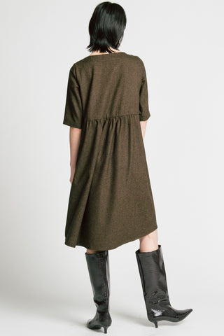 Back view of woman standing in front of grey background wearing brown herringbone llison Wonderland knee length dress with black kitten heel boots. 