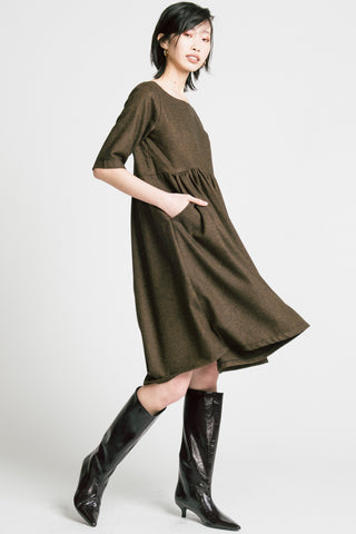 Side view of woman standing in front of grey background wearing brown herringbone llison Wonderland knee length dress with black kitten heel boots. 
