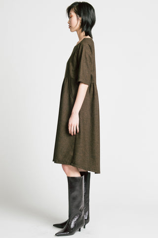 Side view of woman standing in front of grey background wearing brown herringbone llison Wonderland knee length dress with black kitten heel boots. 