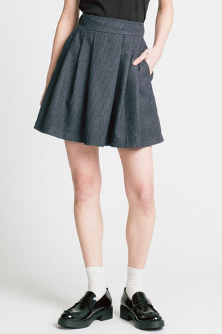 Close-up of woman in front of grey background wearing grey pinstripe Trouble mini skirt by Allison Wonderland with white socks and black patent loafers. 