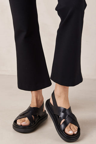 Woman wearing black pants and black leather Trunca sandals by Alohas. 