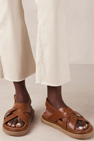 Woman wearing cream pants and tan leather Trunca sandals by Alohas. 