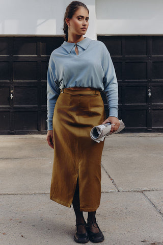 Woman standing outside wearing light blue collared shirt and khaki green A-line midi length Carmine Skirt by Andrea G. 