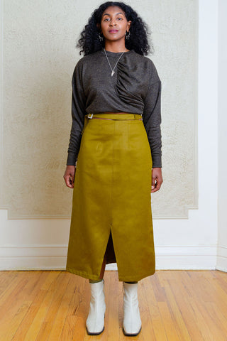 Woman standing in front of wallpapered wall wearing dark grey shirt and green A-line midi length Carmine Skirt by Andrea G. 