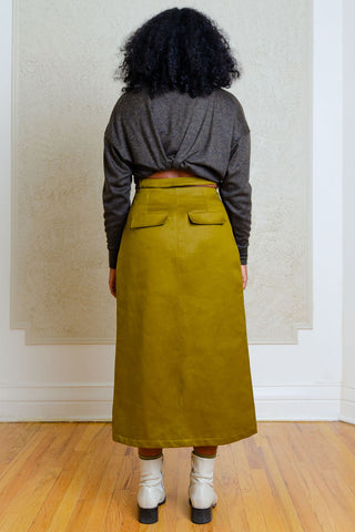 Back view of woman standing in front of wallpapered wall wearing dark grey shirt and green A-line midi length Carmine Skirt by Andrea G. 