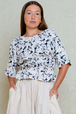 Woman in front of white wall wearing blue and white printed top with voluminous beige pants. 