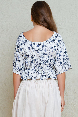 Back view of woman in front of white wall wearing blue and white printed top with voluminous beige pants. 
