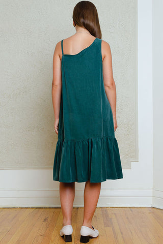Back view of woman wearing green knee length dress with assymetrical neckline and gathered hem. 