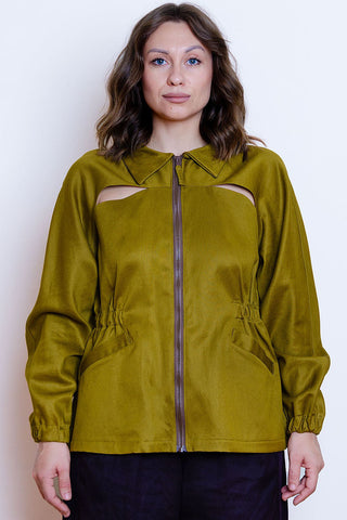 A woman wearing a khaki jacket with a front zipper, elastic detail on waist, and cutout details on the chest, paired with dark pants, set against a plain white background.