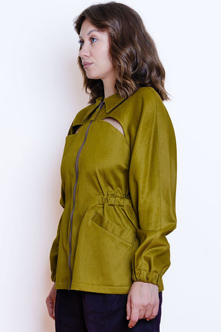 A woman wearing a khaki jacket with a front zipper, cutout detail, and elastic panels at waist, shown in profile against a plain white background.