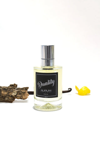 A 50ml glass bottle of Aurum Duality perfume in front of white background, styled with lemon peel, vanilla pod and piece of wood. 