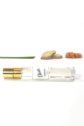 Bottle of Aurum Elixir perfume in front of white background with ginger, lemongrass and wood. 