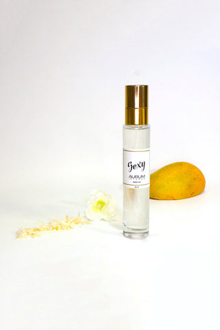 A 30ml glass bottle of Aurum Sexy perfume in front of white background with mango, white flower. 