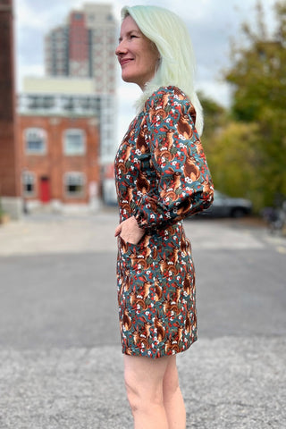 Side view of woman standing outside with long sleeve fitted squirrel print above knee dress. 