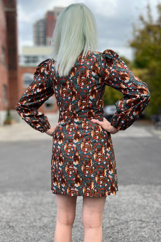 Back view of woman standing outside with long sleeve fitted squirrel print above knee dress. 