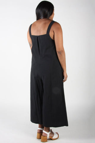 Back view of woman wearing relaxed fit black cotton Dusky Greygone jumpsuit by Birds of North America. 