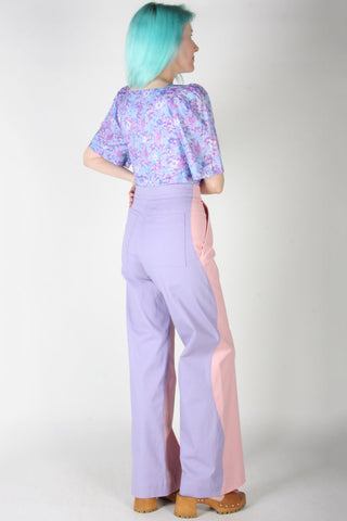 Back view of woman wearing pink and purple wavy side seam Grass Owl pants by Birds of North America. 
