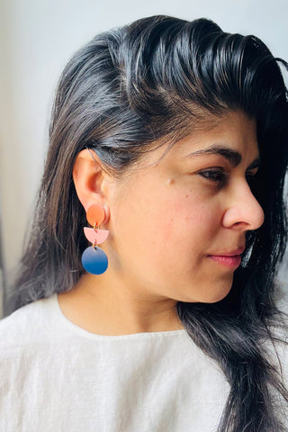 Woman wearing orange, pink and navy leather earrings. 