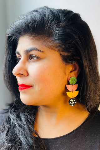 Side view of woman wearing colourful leather earrings made of two circles & two semi-circles. 