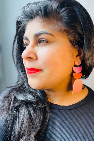 Woman wearing colourful leather earrings with semi circles & larger arch. 