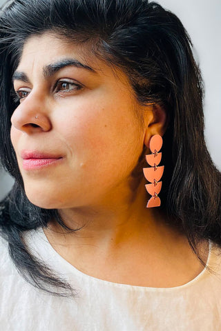 Woman wearing pink dangle earrings made from various leather shapes. 
