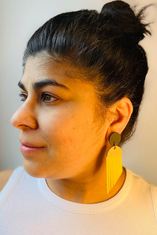 Woman wearing black, pink and yellow leather earrings. 