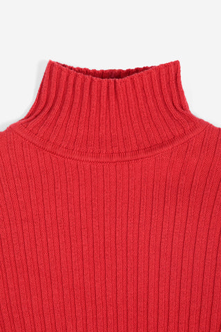 A close-up of a bright red ribbed knit turtleneck sweater, showing the detailed vertical ribbing and collar, set against a plain light gray background.
