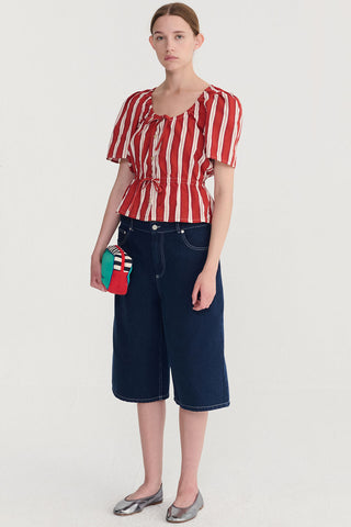 Woman wearing red stripe blouse and dark denim bermuda shorts with contrast stitching. 